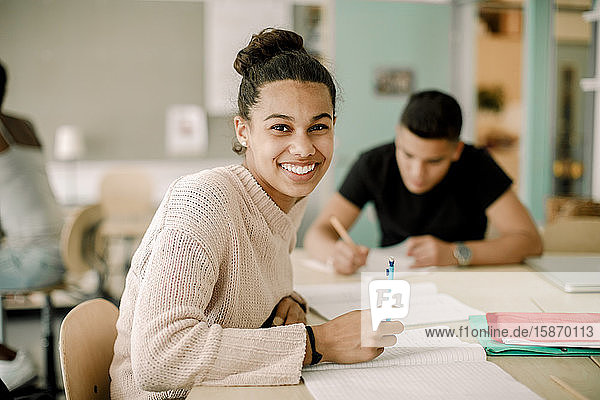 Portrait of smiling teenage girl studying while sitting in classroom