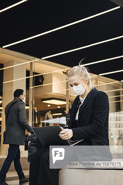 Geschäftsfrau mit Gesichtsmaske sitzt mit Laptop im Freien