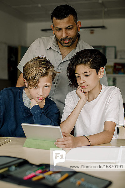 Männlicher Tutor mit Studenten  die ein digitales Tablet benutzen  während sie im Klassenzimmer sitzen