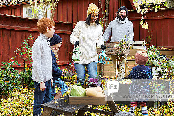 Männer und Frauen sammeln frische Produkte aus dem Garten  während Kinder im Hof stehen