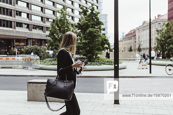 Seitenansicht einer Unternehmerin mit einem Smartphone auf dem Bürgersteig