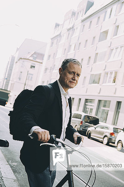 Älterer Geschäftsmann hält Fahrrad auf Straße gegen Gebäude in Stadt