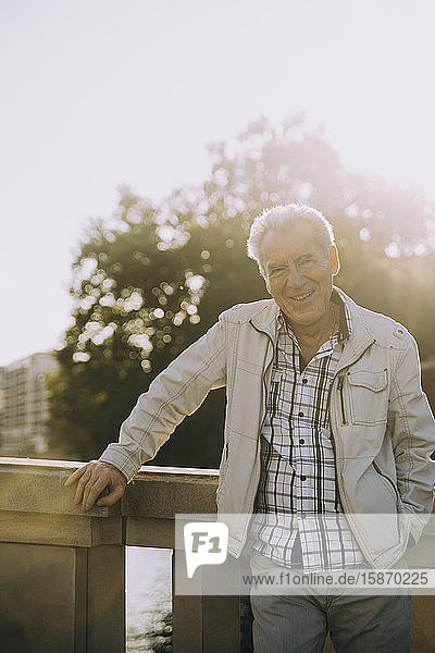 Porträt eines lächelnden älteren Mannes  der an einem sonnigen Tag in der Stadt am Geländer steht
