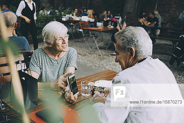 Ältere Frau zeigt einem Mann ein Smartphone  während sie in einem Restaurant in der Stadt sitzt