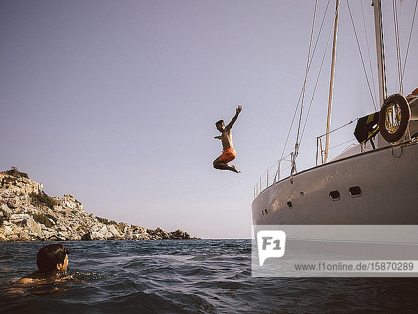 Mann springt in voller Länge vom Boot ins Meer gegen den Himmel
