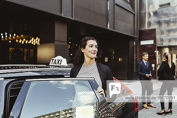 Lächelnde Unternehmerin  die beim Einsteigen in ein Taxi wegschaut