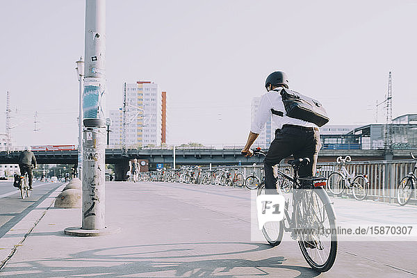 Rückansicht eines Geschäftsmannes auf dem Fahrrad auf dem Bürgersteig vor klarem Himmel in der Stadt