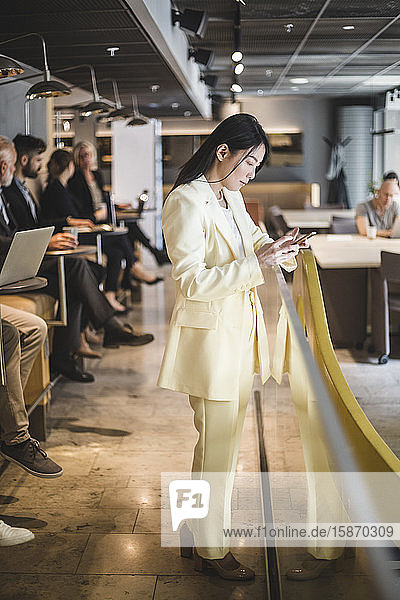 Geschäftsfrau in voller Länge  die im Büro stehend ein Mobiltelefon benutzt