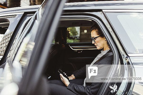 Unternehmer  der ein Smartphone benutzt  während er im Auto sitzt
