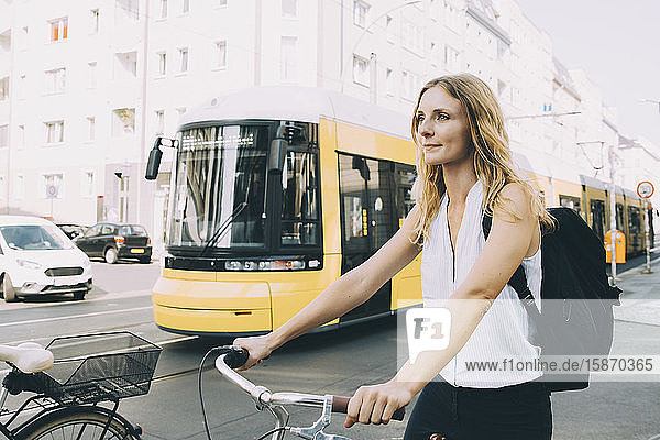Junge Geschäftsfrau mit Fahrrad steht in der Stadt auf der Straße