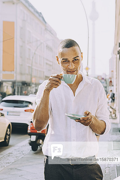 Portrait of businessman drinking coffee on sidewalk cafe in city