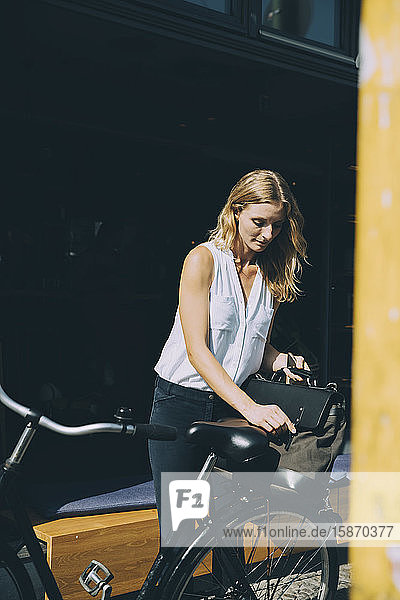 Junge Geschäftsfrau hält Tasche auf Fahrrad auf Straße in Stadt