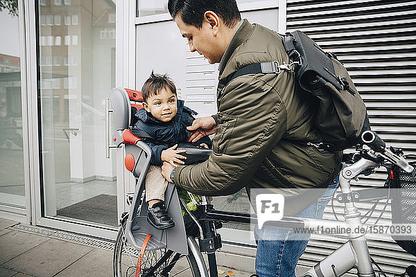 Vater hält Sohn im Sicherheitssitz eines Fahrrads auf dem Bürgersteig in der Stadt