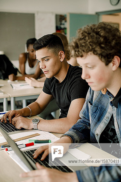 Männliche Studenten benutzen Laptop  während sie im Klassenzimmer am Tisch sitzen