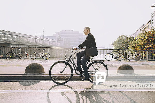 Seitenansicht eines Geschäftsmannes mit dem Fahrrad auf der Straße in der Stadt gegen den Himmel