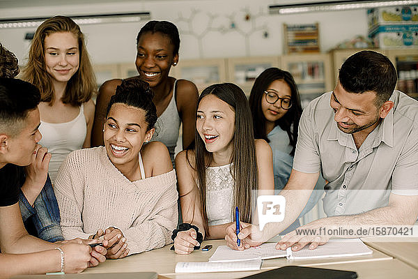 Lächelnde Schüler schauen einen Teenager an  während der Lehrer im Klassenzimmer über dem Tisch unterrichtet