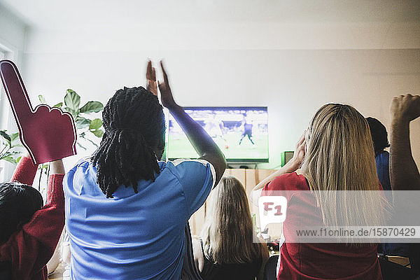 Rückansicht von aufgeregten Fussballfans  die mit Freunden zu Hause ein Spiel sehen