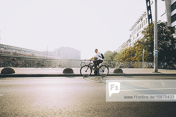 Geschäftsmann mit Rucksack in voller Länge mit dem Fahrrad auf der Straße in der Stadt gegen den Himmel