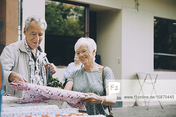 Lächelnde ältere Frau zeigt einem Mann beim Einkaufen auf dem Markt in der Stadt Textilien