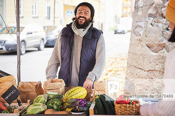 Lächelnder Mann kauft am Obststand frisches Gemüse von einer Marktverkäuferin