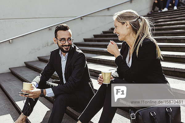 Lächelnde Geschäftsleute mit Kaffee auf der Treppe sitzend