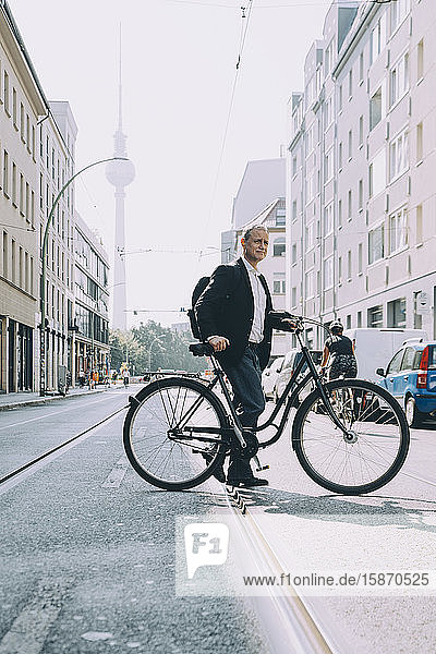 Full length of businessman with bicycle on road in city