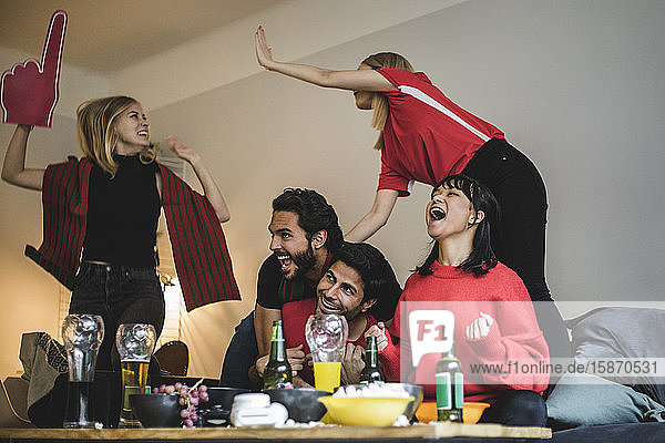 Glückliche männliche und weibliche Fans feiern  während sie zu Hause ein Fußballspiel sehen