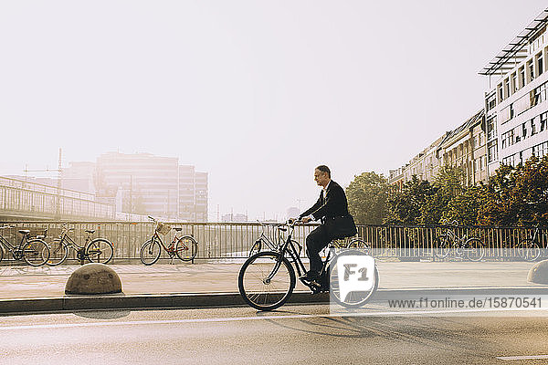 Fahrradfahren in voller Länge eines reifen Mannes auf Straße in Stadt gegen Himmel