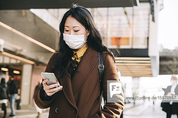 Frau geht auf der Straße mit Gesichtsmaske und Smartphone