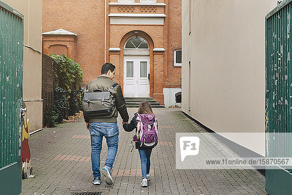 Rückansicht von Vater und Tochter mit Rucksack auf dem Weg zur Schule