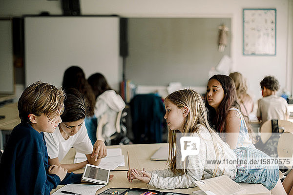 Female student leaning over table while friends sitting in classroom