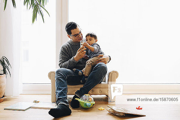 Vater spielt in voller Länge mit Kleinkind Sohn  während er zu Hause auf dem Sofa sitzt