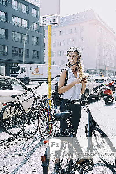 Geschäftsfrau in voller Länge mit Fahrrad auf der Straße in der Stadt stehend