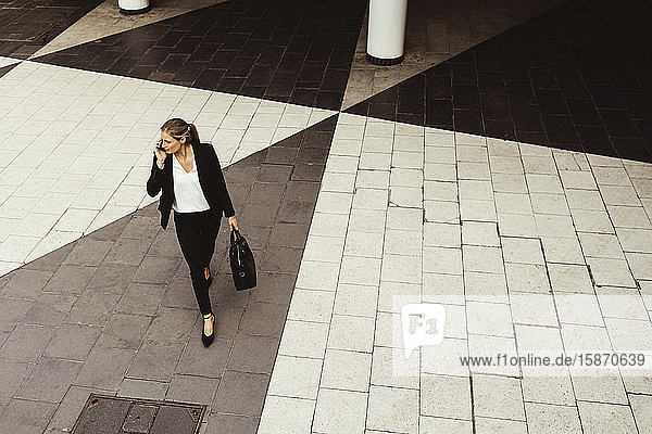 High angle view of businesswoman talking through phone while walking on street