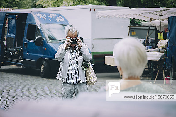 Senior tourist taking photograph of woman while standing in city