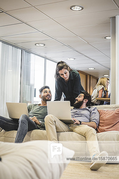 Junge Geschäftsleute arbeiten am Laptop  während sie mit einer Mitarbeiterin im Büro diskutieren