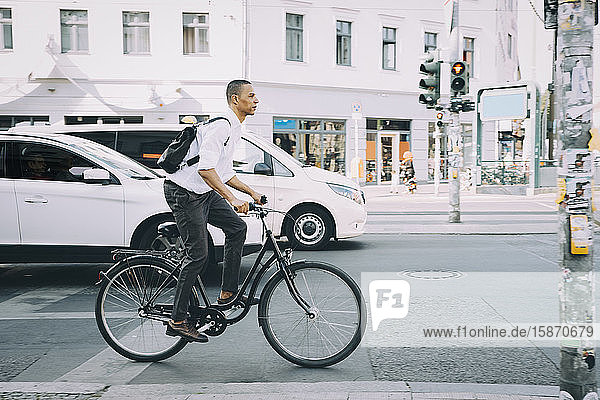 Fahrrad fahrender Geschäftsmann in voller Länge auf Bürgersteig gegen Gebäude in der Stadt