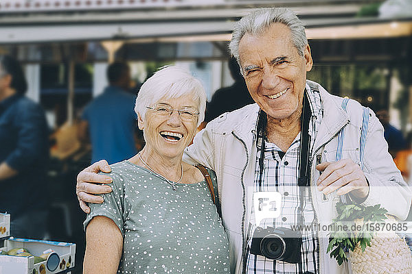 Porträt eines lächelnden älteren Paares mit Arm um den Arm auf dem Markt in der Stadt stehend