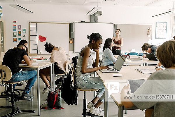 Schüler der Junior High studieren  während eine Lehrerin im Klassenzimmer steht