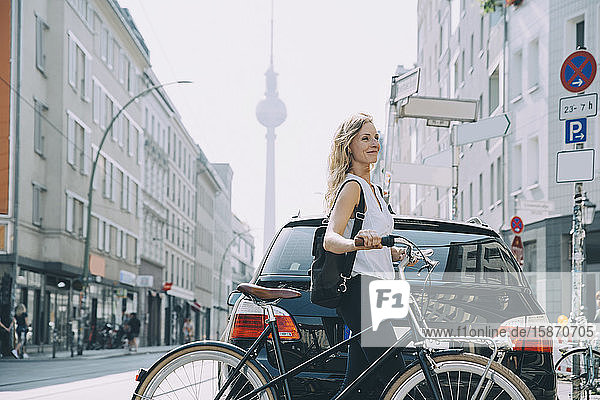 Lächelnde junge Frau mit Rucksack fährt Fahrrad auf der Straße in der Stadt