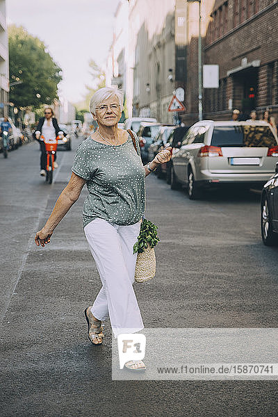 Full length portrait of woman walking on sidewalk in city