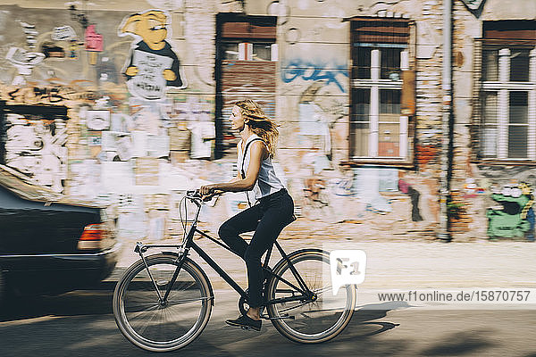 Seitenansicht einer jungen Geschäftsfrau auf dem Fahrrad gegen Gebäude in der Stadt