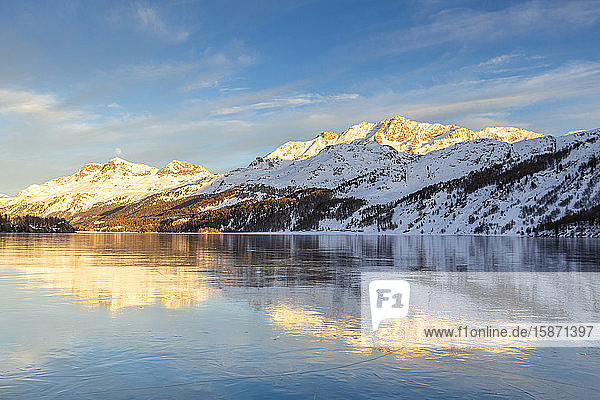 Mountains illuminated by sun at sunset reflected on the icy surfaces of Lake Sils Engadine Graubunden Switzerland Europe