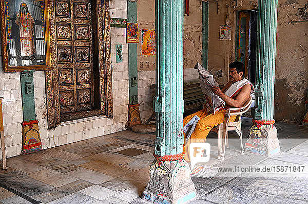 Hindu priest reading the daily newspaper at an old backstreet temple in the palls (alleyways) of old Ahmedabad  Gujarat  India  Asia