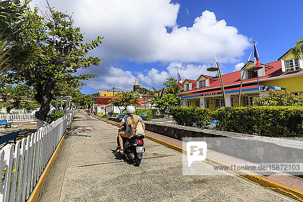 Paar auf Moped  bunte Stadt Bourg des Saintes  Terre de Haut  Iles Des Saintes  Les Saintes  Guadeloupe  Inseln unter dem Winde  Westindien  Karibik  Mittelamerika