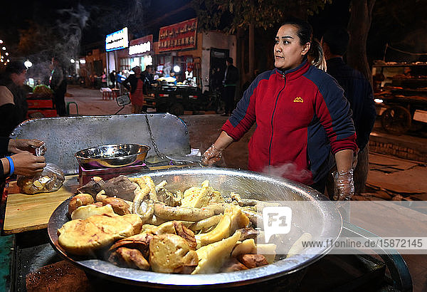 Frau verkauft gekochtes Fleisch an einem Rikscha-Stand auf dem Turfan-Nachtmarkt  Turfan  Xinjiang  China  Asien