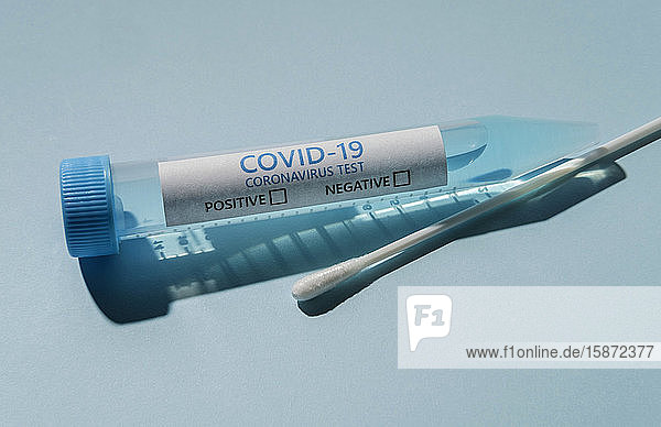 Covid-19 Testfläschchen und Tupfer auf blauem Hintergrund