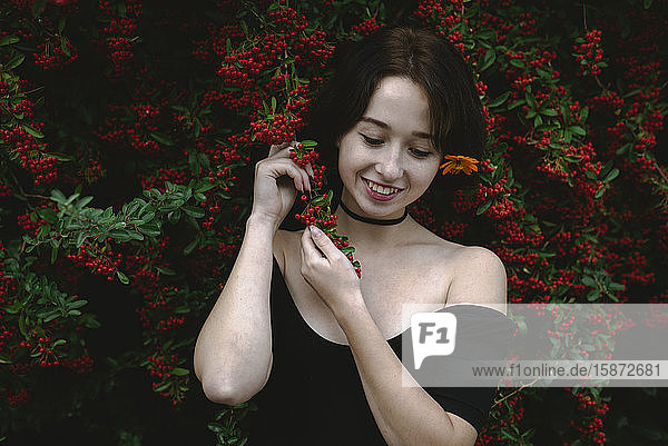 Young woman standing by bush with red berries