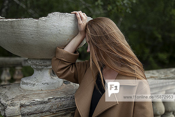 Junge Frau hält zerbrochenen Blumentopf auf steinernem Geländer