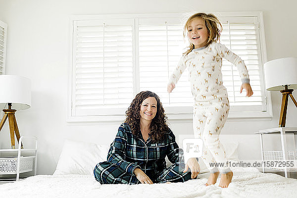 Girl jumping on bed and her smiling mother